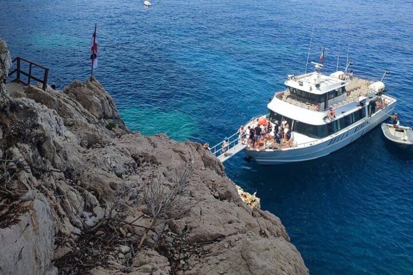A boat docked at a rocky coastline with clear blue water. 1