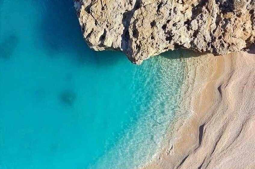 A coastal landscape with clear turquoise waters, a sandy beach, and rocky cliffs. 3