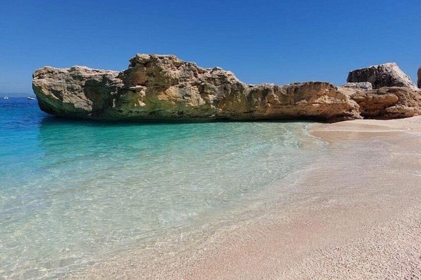 A clear beach with a large rock formation in the water. 5