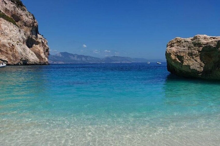 A coastal scene with clear turquoise water, rocky formations, and distant mountains. 5