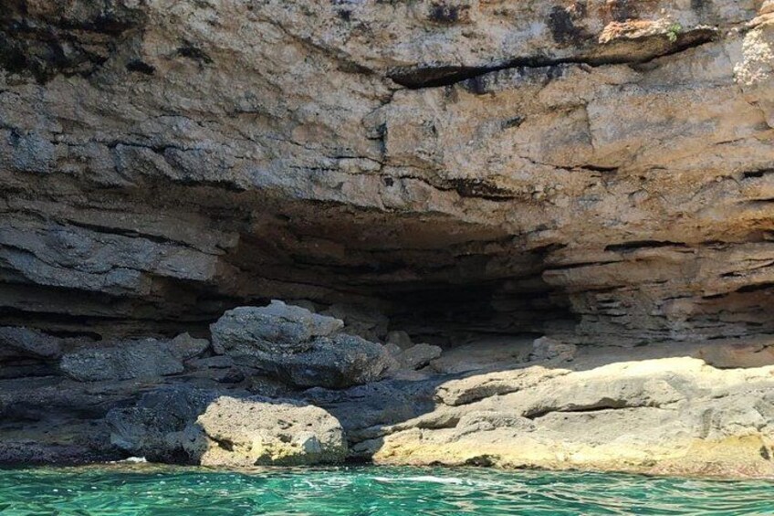 A rocky coastal landscape with layered cliffs and calm turquoise waters. 2