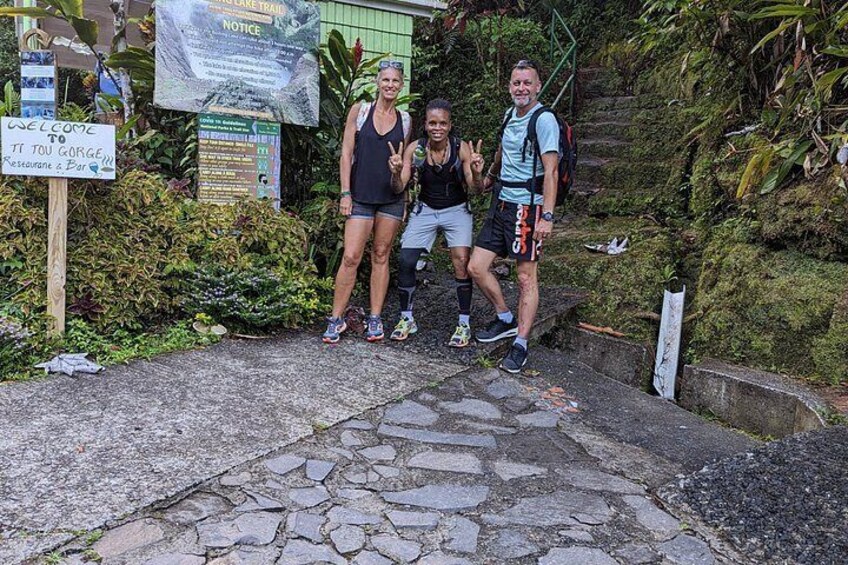 Trois personnes se tiennent sur un chemin de pierre, avec de la verdure et des panneaux en arrière-plan. 2