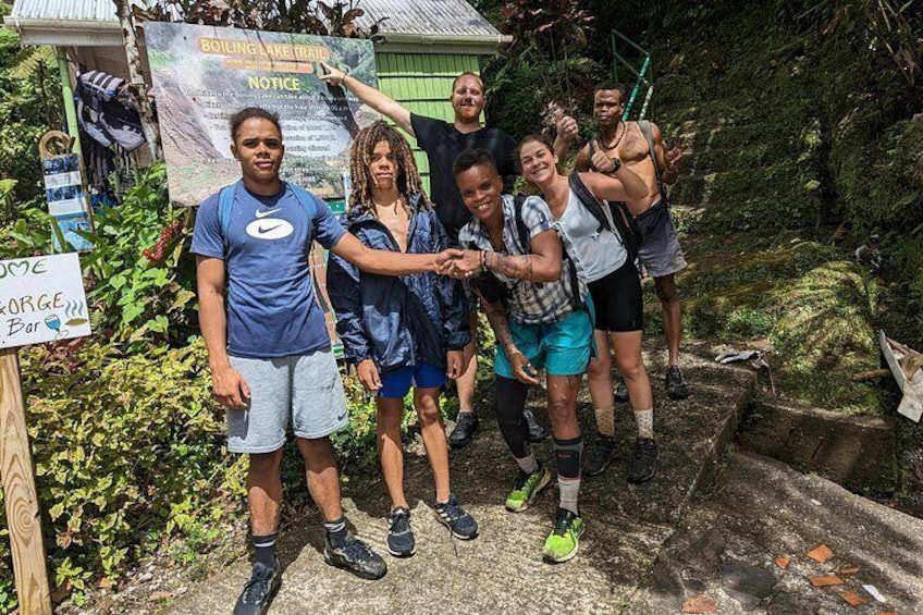 Un groupe de personnes se tient sur un sentier de pierre, à côté d’un panneau indiquant « Sentier menant au lac bouillant » et « Avis ». 3