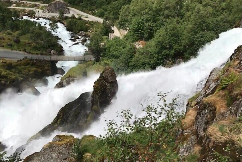 A waterfall cascading over rocks, a bridge, and lush greenery. 2