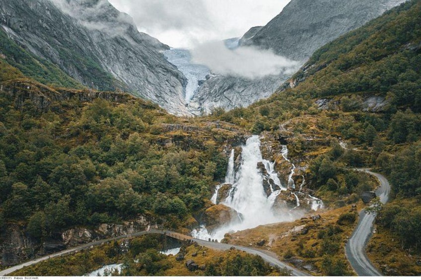 A waterfall cascading down a mountain, surrounded by lush greenery and a winding road. 2