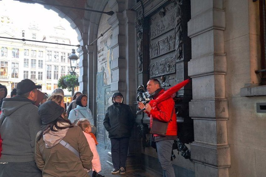 A street scene with a crowd of people, a man in a red jacket, and a building with detailed carvings. 2