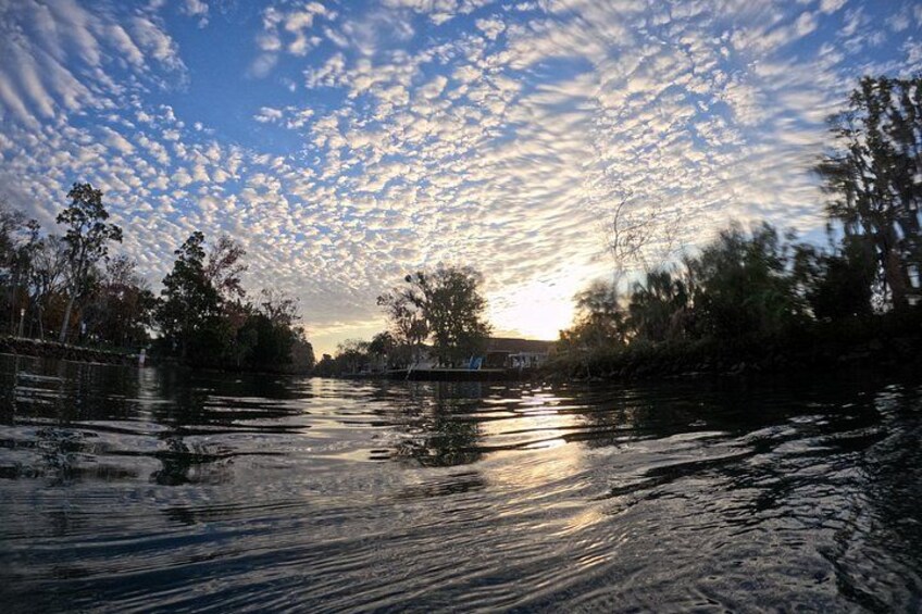 A river with trees on the banks, a boat in the water, and a sunset with clouds in the sky. 2