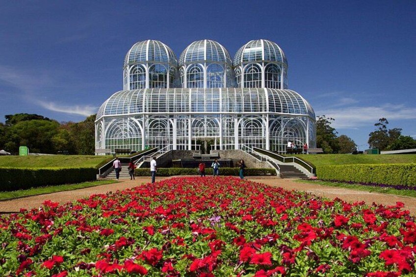 A glasshouse with domed structures, surrounded by a garden of red flowers. 5