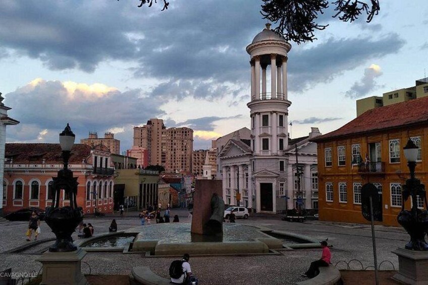 A historic square with a central fountain, a prominent clock tower, and surrounding buildings. 3