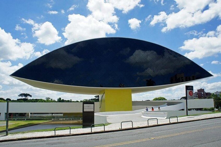 A large, modern structure with a curved roof, a yellow base, and a reflective surface. 4