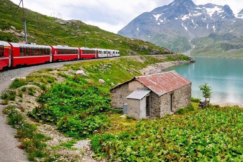 Ett rött tåg på rälsen, en liten stenbyggnad och en sjö med berg i bakgrunden. 3