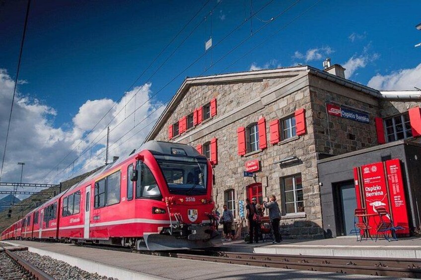 Ett rött tåg vid en station med en byggnad av sten och röda markiser. 2