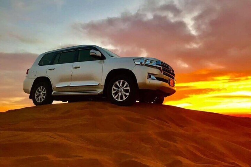A white SUV parked on a sand dune with a sunset in the background. 1