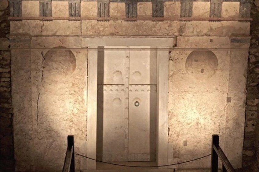 Un muro de piedra con una puerta grande y ornamentada en el centro, flanqueada por dos hornacinas circulares. 1
