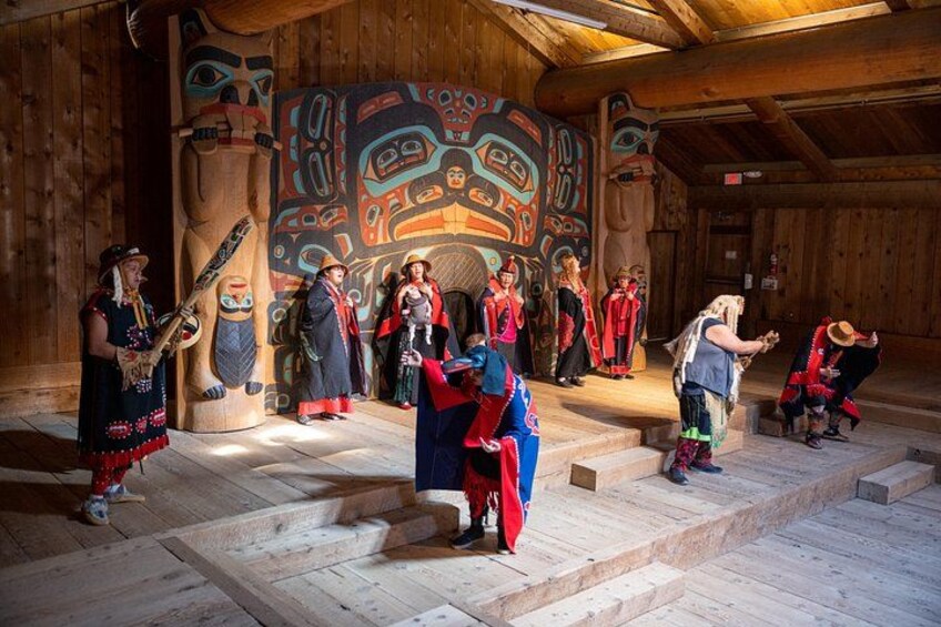 A group of people in traditional attire performing in a wooden building with totemic art. 2
