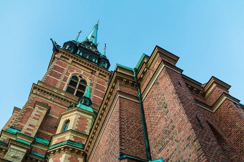 A tall brick building with a clock tower and green spires. 5