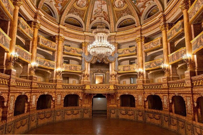 Interior ornamentado de un teatro con una gran araña de cristal, frescos detallados en el techo y varios palcos. 2