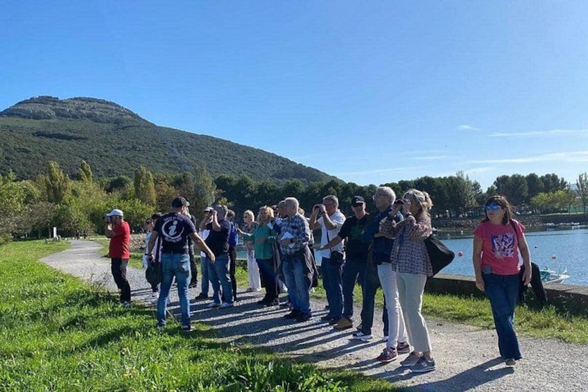 A group of people walking along a path beside a lake with a hill in the background. 4