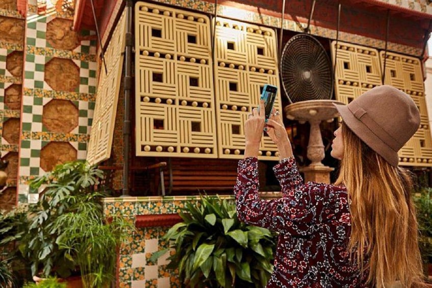 A person taking a photo with a smartphone in front of a decorative wall with geometric patterns and a fan. 4