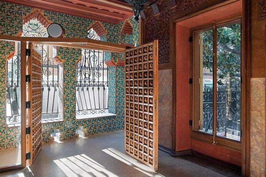 A room with patterned wallpaper, a wooden door, and a window with a metal gate. 3