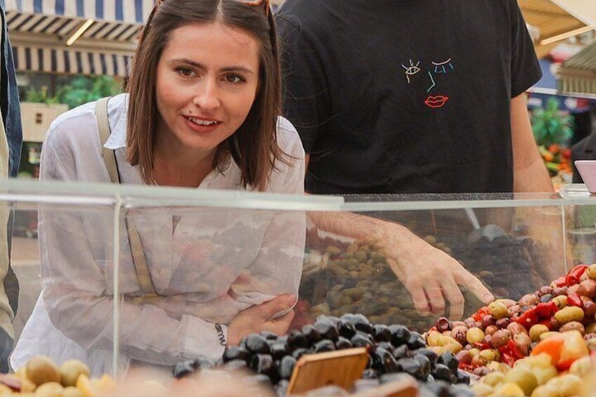 A person in a white shirt and apron behind a glass counter with various fruits and nuts displayed. 2