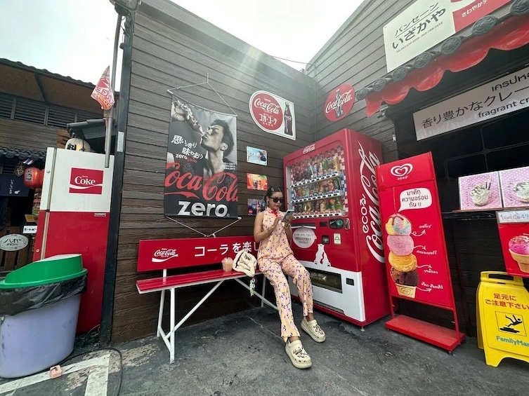 Henkilö istuu penkillä Coca-Cola Zero -automaatin edessä. 3