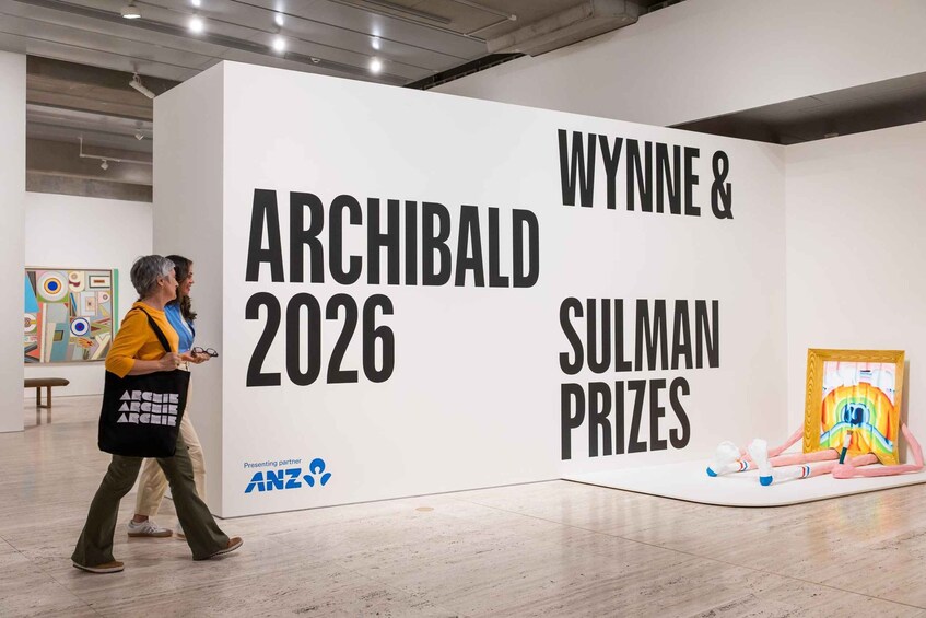 An art exhibition with a large white wall displaying 'ARCHIBALD 2026' and 'WYNN & SULMAN PRIZES'. 3