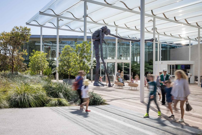 A modern building with a glass facade and a sculpture of a figure reaching upwards. 5