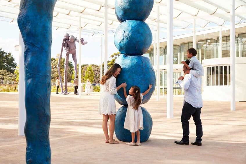 A sculpture of stacked spheres, a glass building, and a statue of a figure in the background. 5