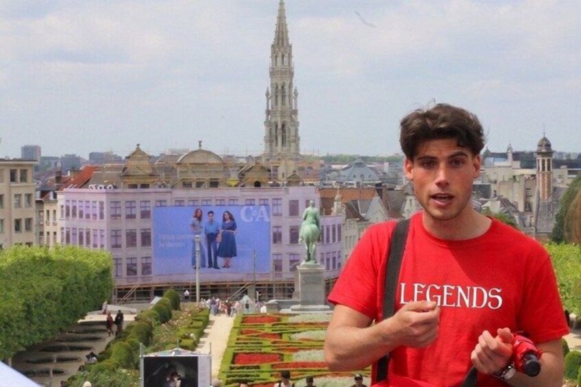Une personne portant un t-shirt rouge avec le mot « LEGENDS » écrit dessus, se tenant dans un jardin avec une vue sur la ville en arrière-plan. 3