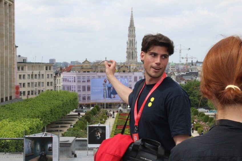 Une personne tenant un sac rouge, debout sur un toit, avec une vue sur la ville en arrière-plan. 1
