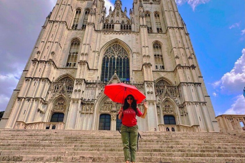 Une personne se tient sur des marches devant une grande cathédrale richement décorée, tenant un parapluie rouge. 5