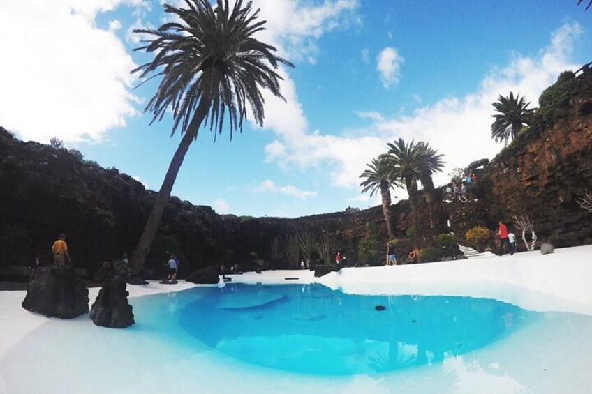 A clear blue pool surrounded by white sand and palm trees on a rocky hillside. 2