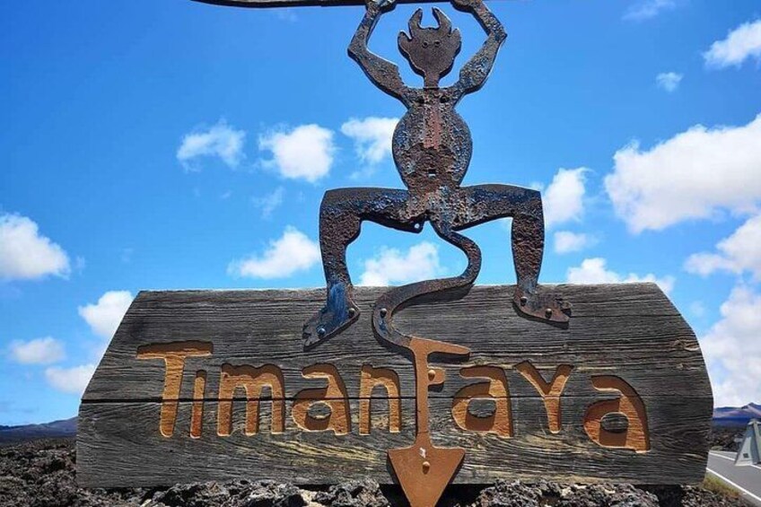 A wooden sign with a metal sculpture of a figure in a dynamic pose, with the name 'Timanfaya' carved on it. 4