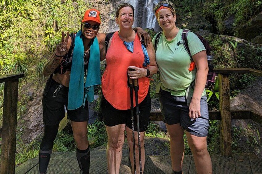 Tres personas sobre un puente de madera, con una cascada al fondo. 3