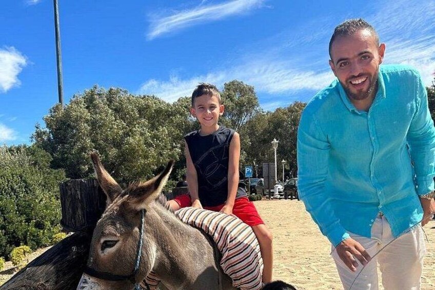 Un burro, una persona con camisa azul y otra persona con camisa negra sentadas junto al burro. 3