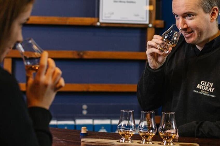 Una persona sosteniendo una copa de whisky, con otras varias copas sobre una mesa. 1