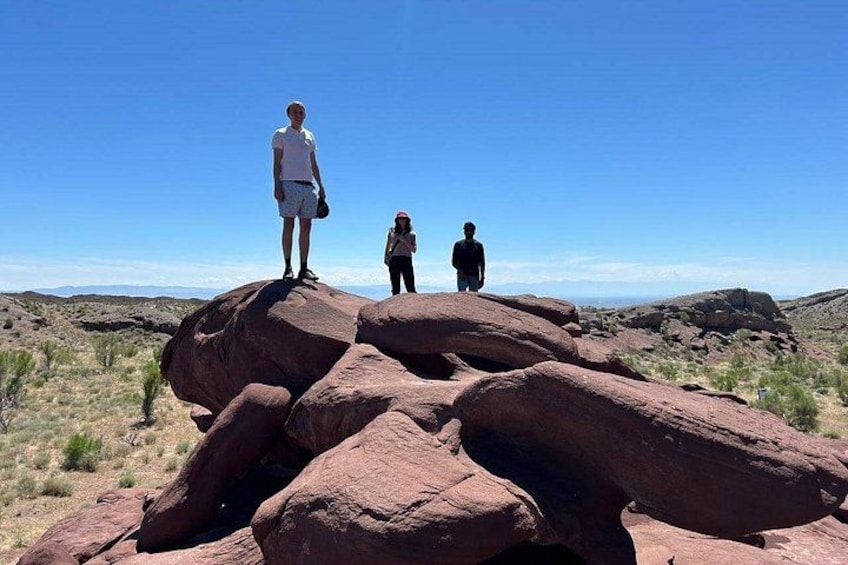 Drei Personen stehen auf großen roten Felsen vor einem wolkenlosen, blauen Himmel. 4