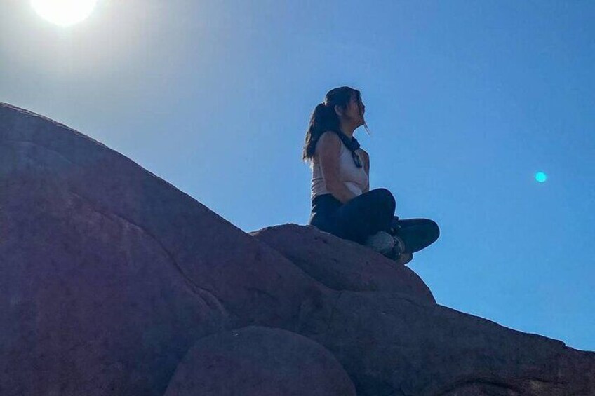 Una persona sentada sobre una roca con el sol al fondo. 2