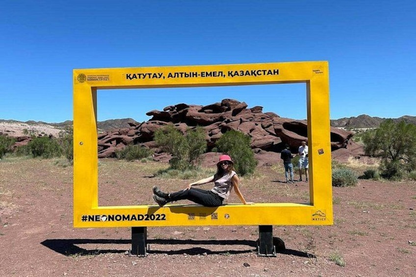 Ein gelbes Schild mit einer darauf sitzenden Person, vor einer Wüstenlandschaft mit roten Felsen und vereinzelter Vegetation. 5
