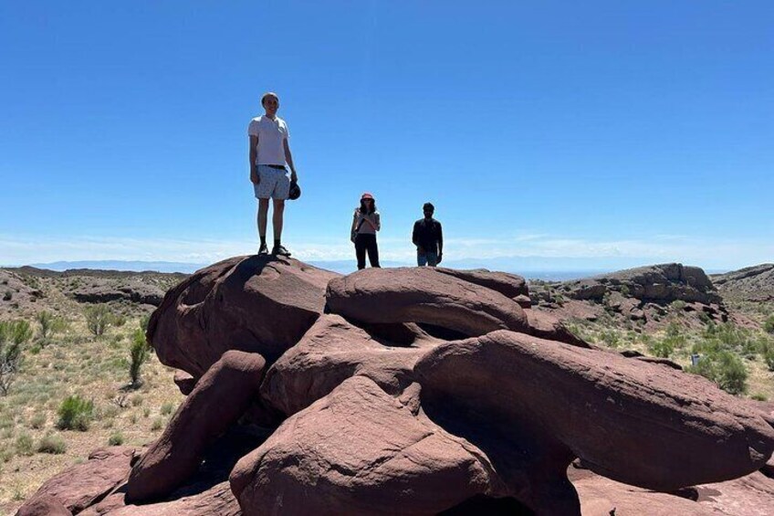 Tres personas sobre rocas rojas enormes en un paisaje desértico. 3
