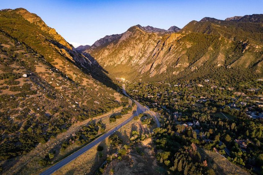Eine gebirgige Landschaft mit einer kurvenreichen Straße durch ein Tal, umgeben von dichten Wäldern und Wohngebieten. 5