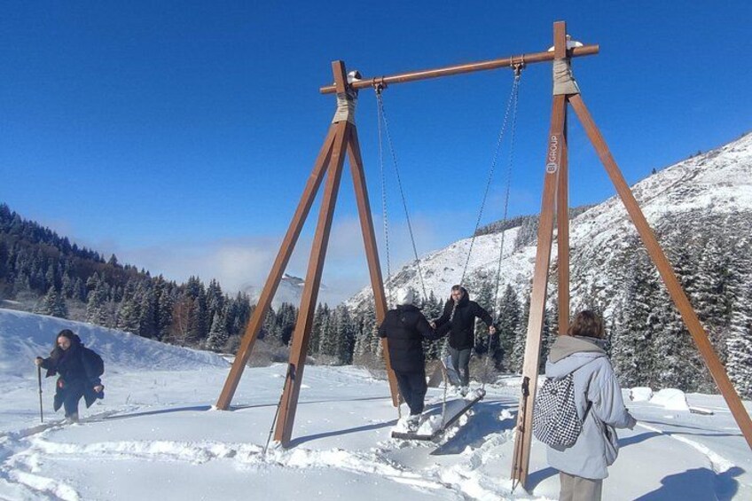 A wooden swing set in a snowy mountainous area with people using it. 5