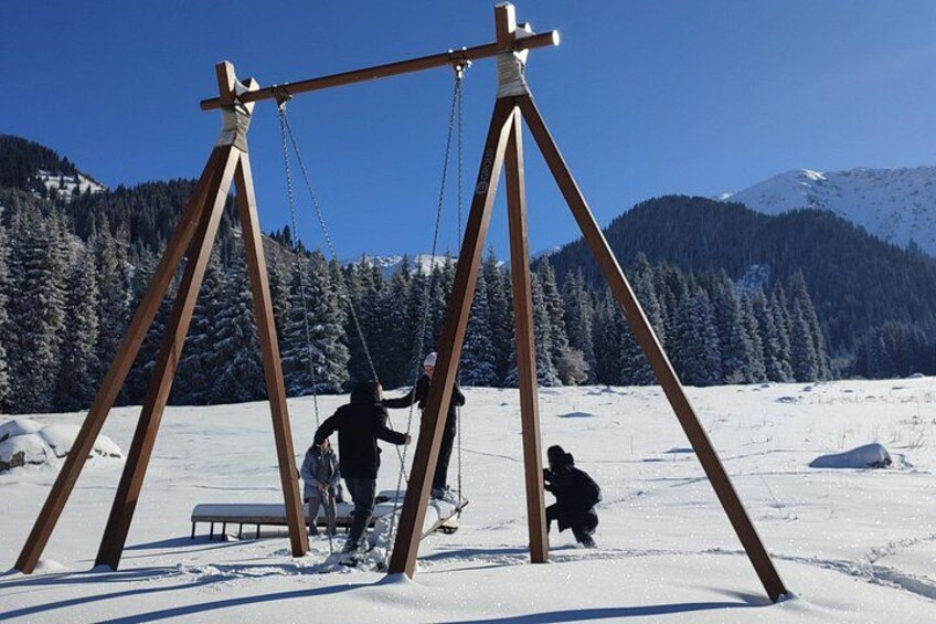 A wooden swing set in a snowy landscape with mountains in the background. 3
