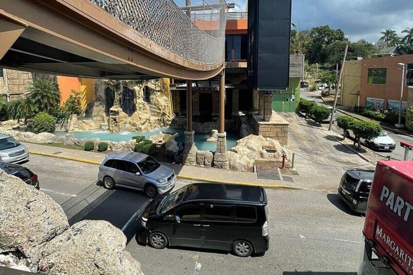 Un parcheggio con auto, un edificio e una formazione rocciosa, e un marciapiede. 3