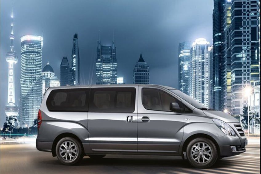 Un minivan argentato parcheggiato in una strada cittadina, con i grattacieli illuminati sullo sfondo. 2