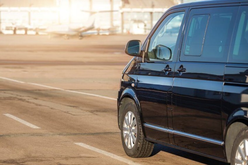 Un SUV nero parcheggiato sul piazzale di un aeroporto, con aerei visibili sullo sfondo. 4