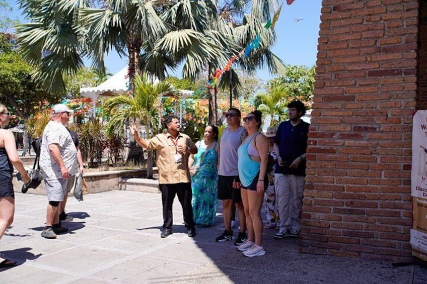 A group of people standing outdoors, some looking at a sign on a brick wall. 3