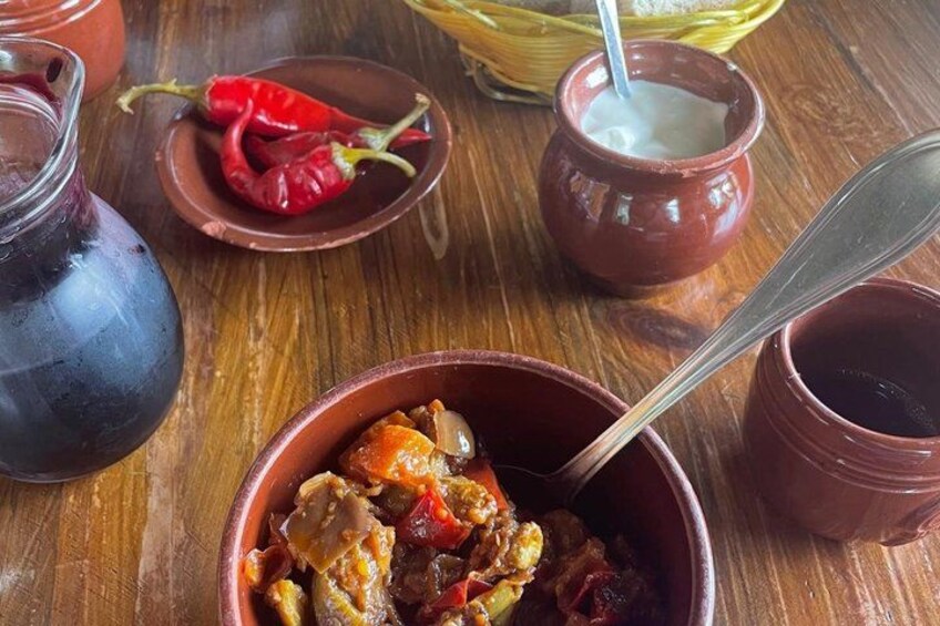 A wooden table with a bowl of stew, a jug of liquid, and a small bowl with a red chili pepper. 2