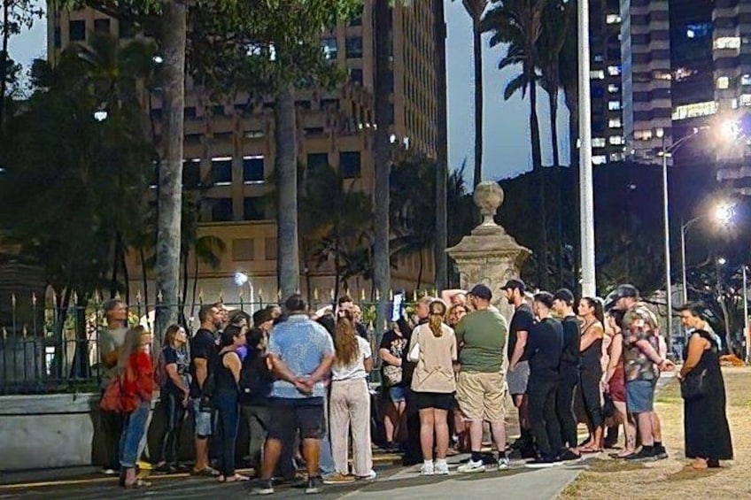 A group of people gathered around a fountain in an urban park at night. 3